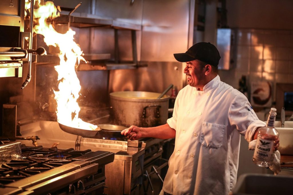 Chef in white uniform cooking over a high flame in the restaurant kitchen