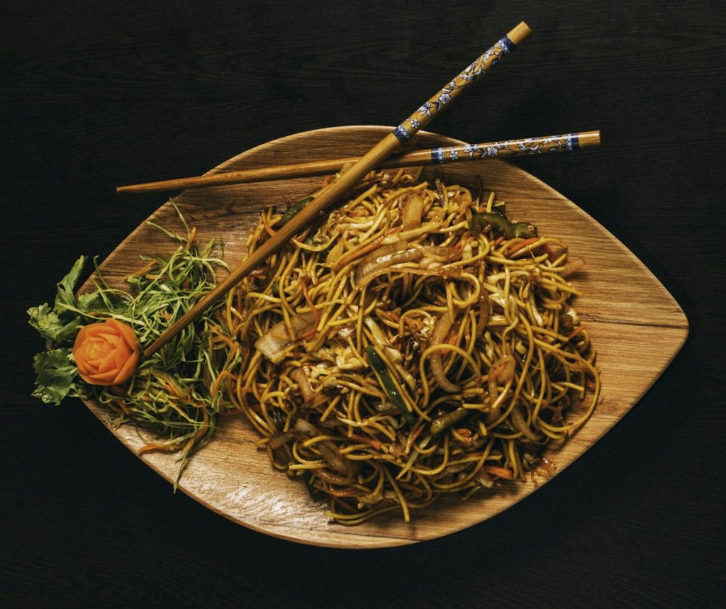 Stir-fried chow mein noodles with vegetables and chopsticks on a wooden platter