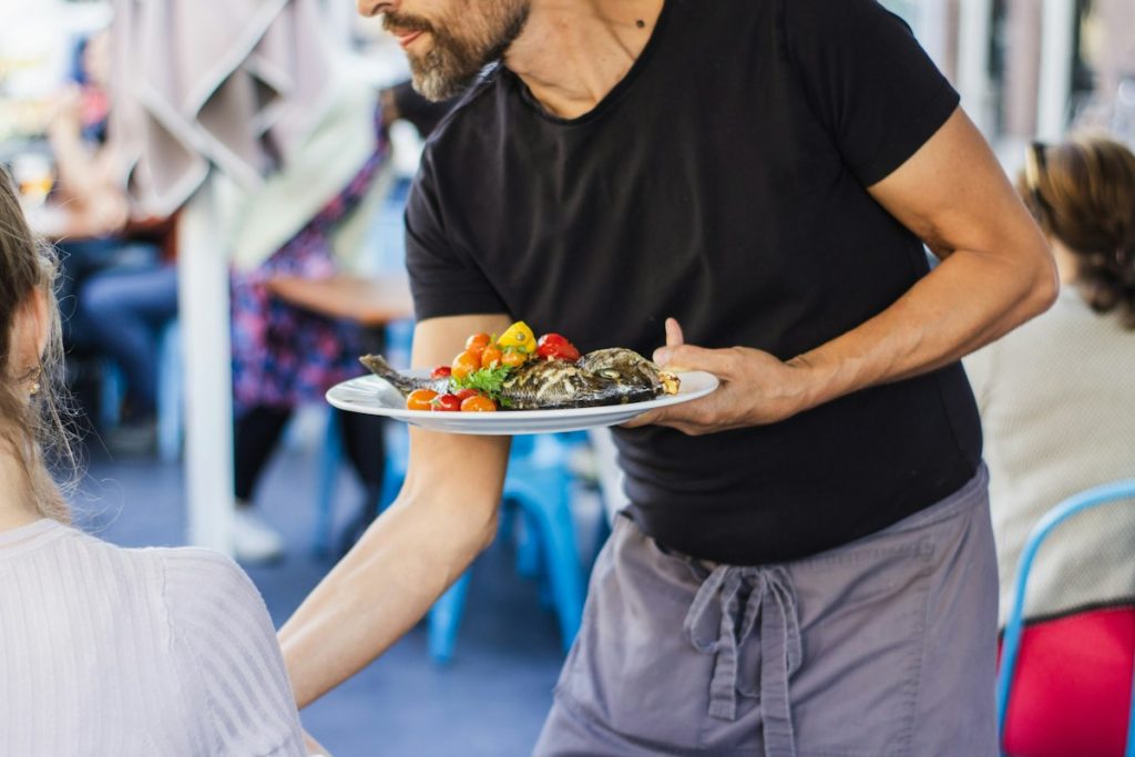 Server carrying a freshly plated dish through the dining room